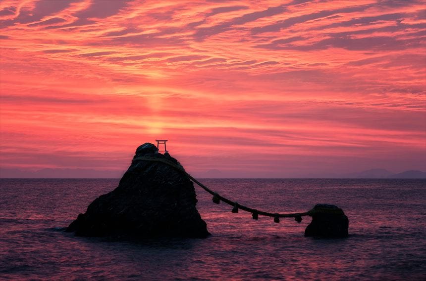 日の出前の瀑焼けの空と伊勢の夫婦岩の間に富士山のシルエット。