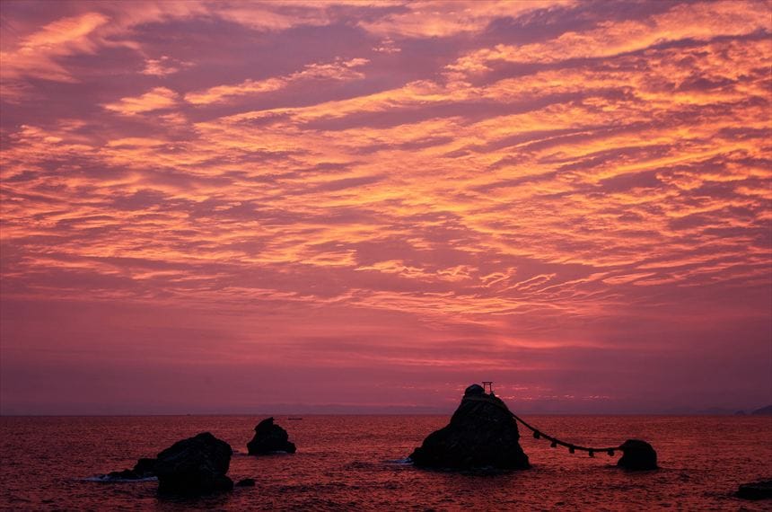日の出前の爆焼けの空と伊勢の夫婦岩の間に富士山のシルエット。空には富士山の影