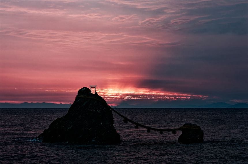 日の出前の爆焼けの空と伊勢の夫婦岩の間に富士山のシルエット。空には富士山の影